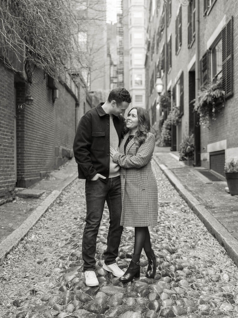 Couple stands facing each other on Acorn Street cobblestones during Beacon Hill engagement photos