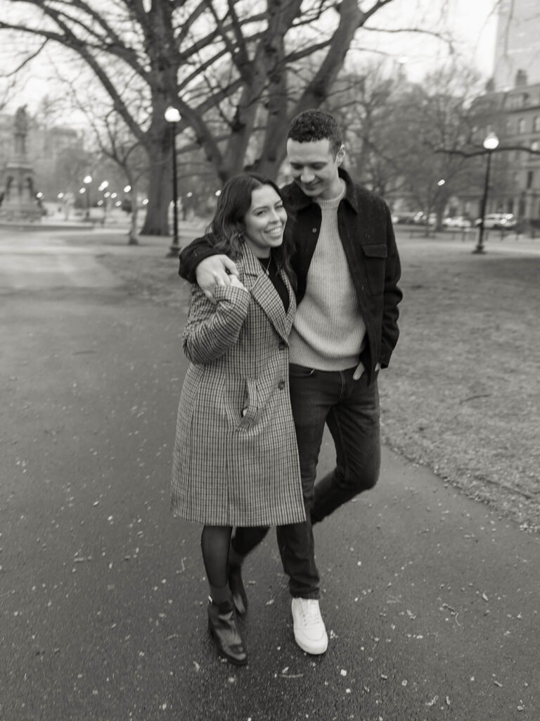 Alyssa and Jason walk toward the camera on a park path with his arm around her during engagement photos