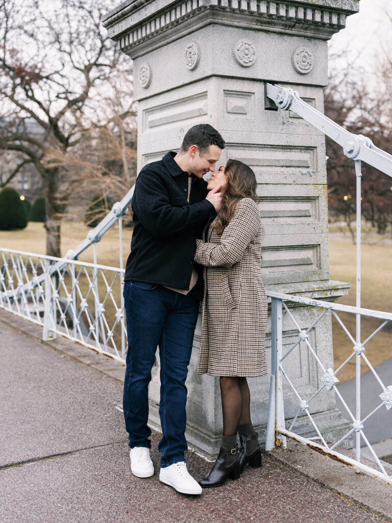 Couple face each other as if about to kiss at a stone bridge pillar during engagement photos in Boston Public Garden.