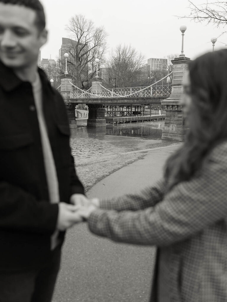 Bride & groom stand out of focus holding hands with the pedestrian bridge in focus in the background