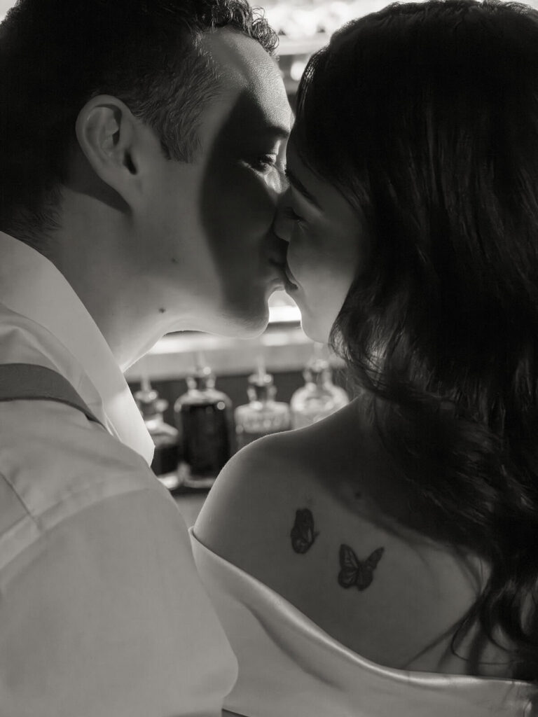 Black and white close-up of couple about to kiss showing butterfly tattoos on upper back
