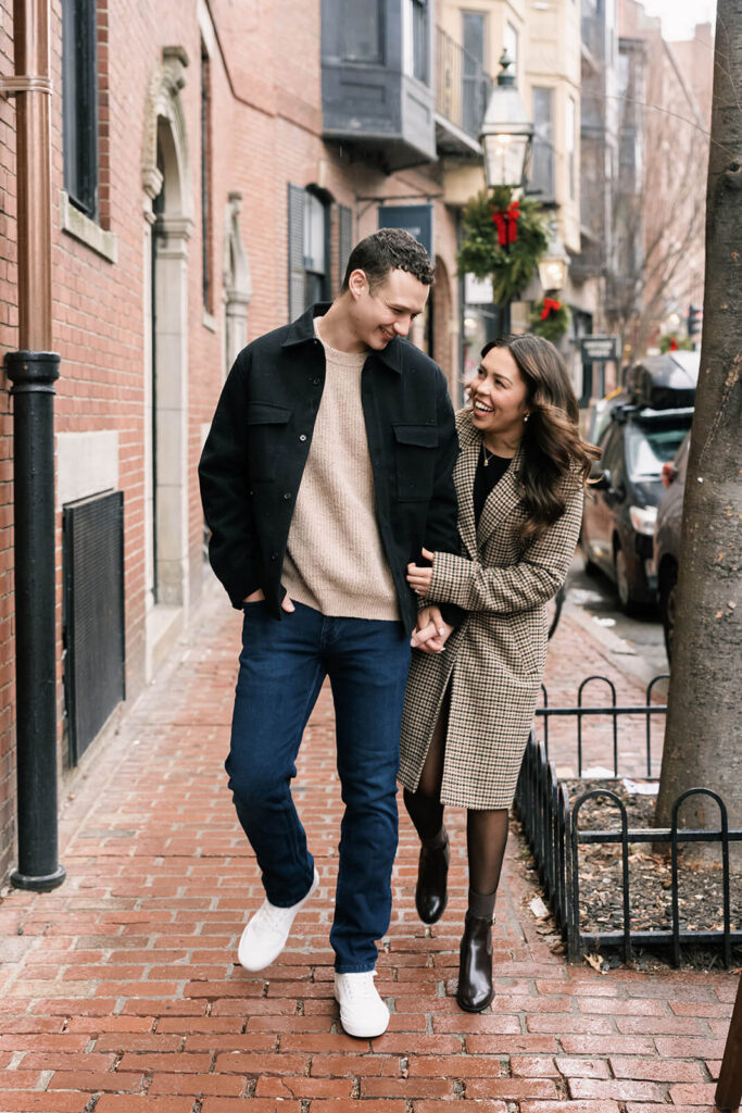Couple walking arm-in-arm laughing on brick sidewalk in Beacon Hill with holiday wreaths