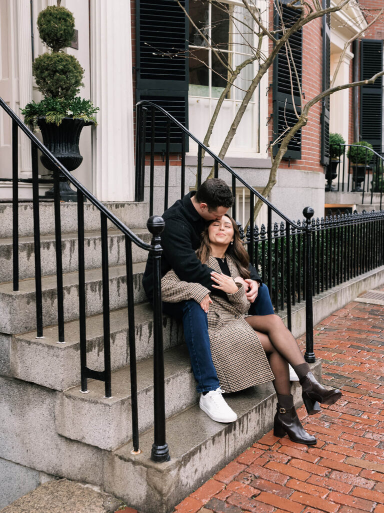 Man kissing woman's forehead on brownstone steps with iron railings Beacon Hill engagement session