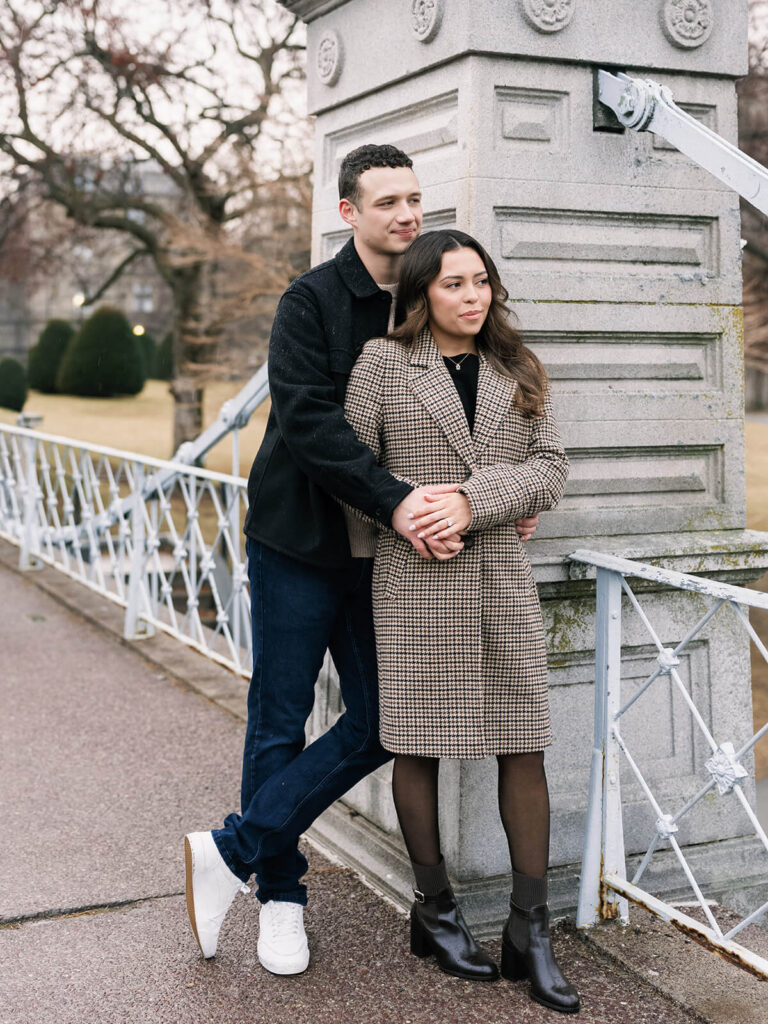 Couple embracing by stone bridge pillar in Boston Public Garden during winter engagement session