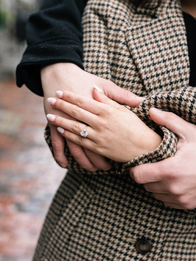 Close-up of couple's hands intertwined showing engagement ring and houndstooth coat sleeve