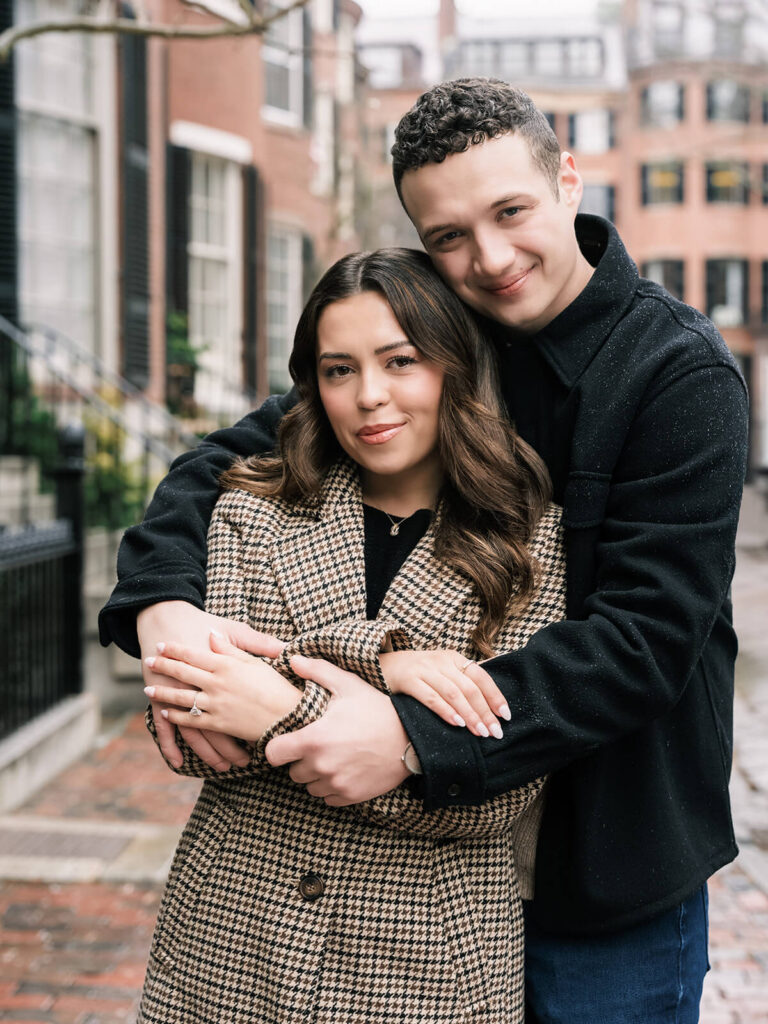 Couple facing camera with man embracing woman from behind on Beacon Hill brick sidewalk