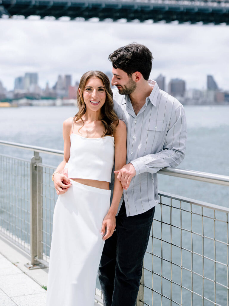 Engaged couple at Domino Park Brooklyn with Williamsburg Bridge spanning overhead