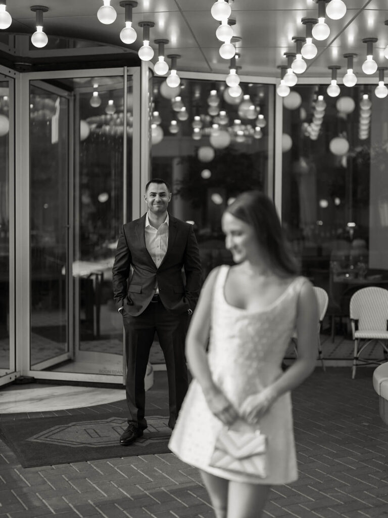 Man in dark suit smiling at woman walking ahead at hotel entrance Charlotte engagement photos