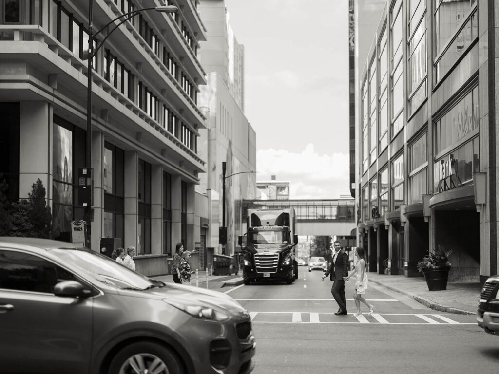 Black and white wide shot of couple crossing downtown Charlotte street with buildings around them