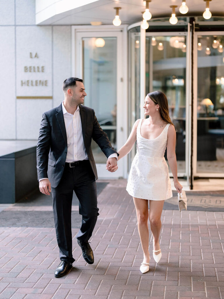 Couple walking hand-in-hand on brick sidewalk outside La Belle Helene Charlotte engagement photos