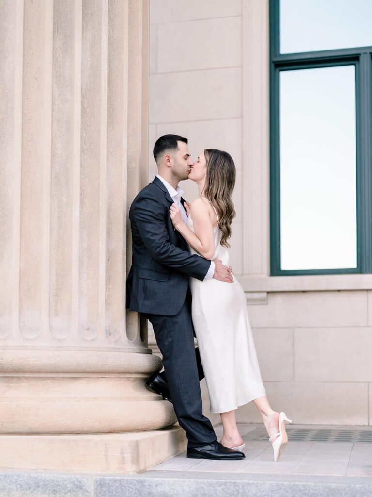 Couple kissing against stone column with foot raised outside columned building Gandhi Park Charlotte