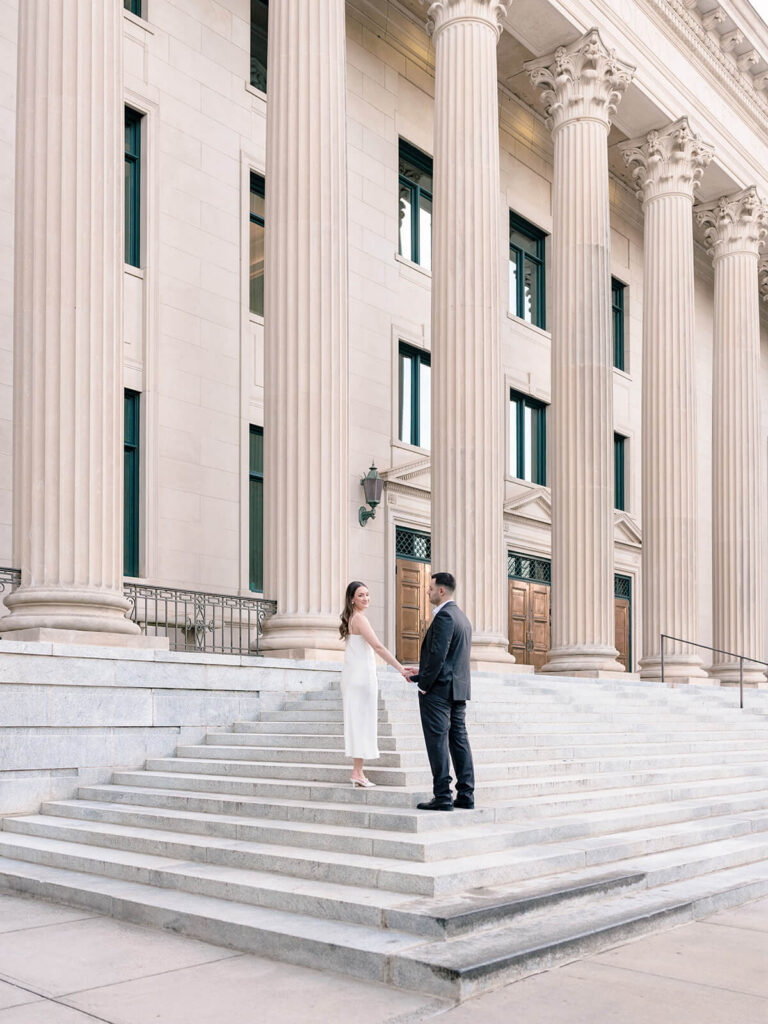 Couple holding hands on stone steps of neoclassical building with Corinthian columns Gandhi Park