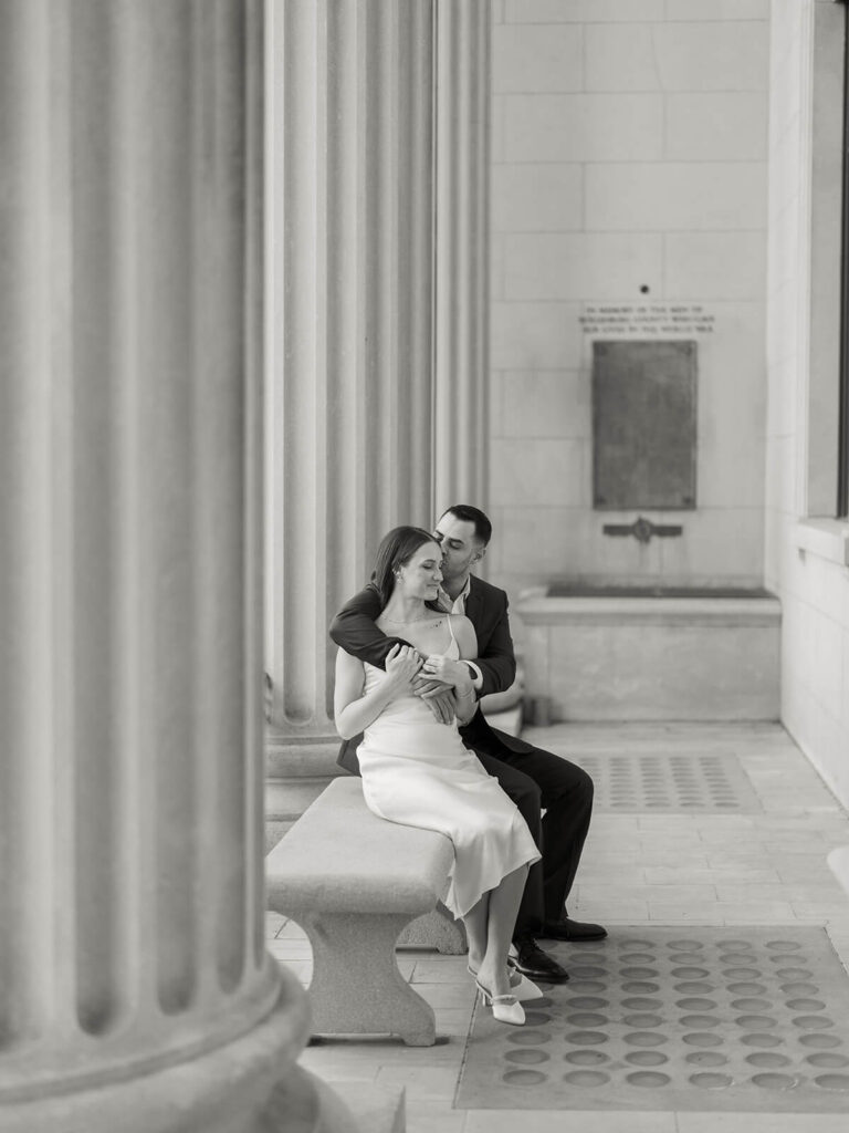 Black and white of couple embracing on stone bench between columns Gandhi Park Charlotte