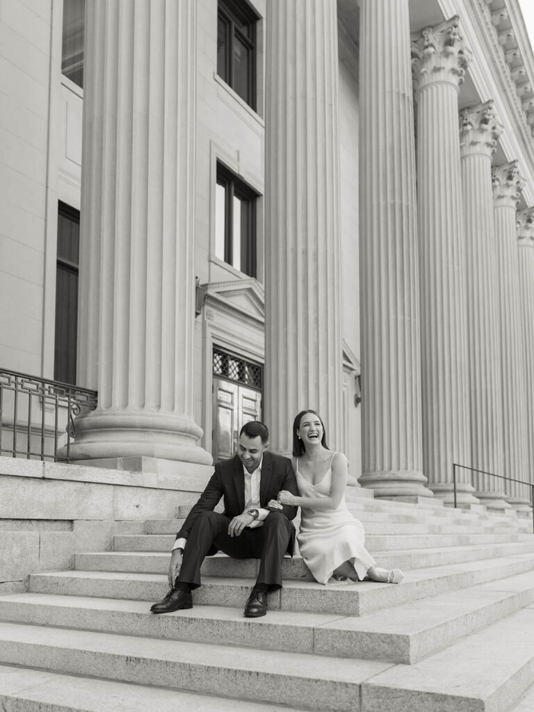 Black and white of couple laughing on steps of columned building Gandhi Park Charlotte engagement
