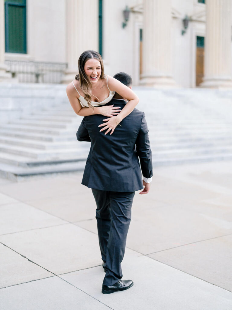 Man carrying laughing woman over his shoulder outside columned building Gandhi Park Charlotte