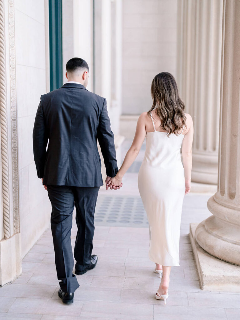 Back view of couple walking hand-in-hand through columned corridor Gandhi Park Charlotte