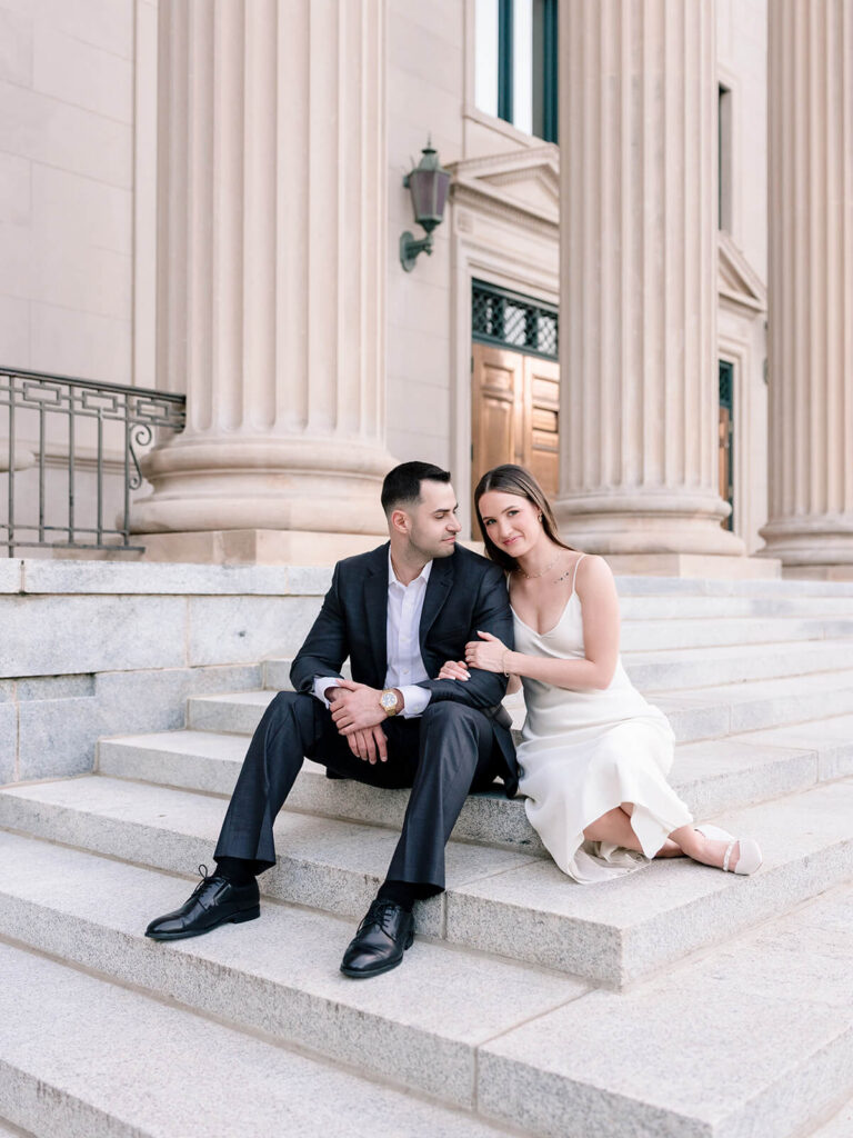 Couple sitting on stone steps of classical building with columns Gandhi Park engagement photos