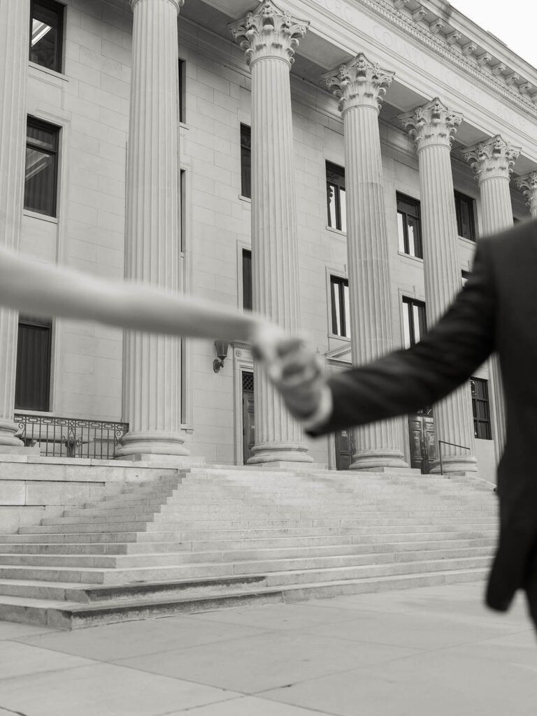 Close-up of couple holding hands with neoclassical Corinthian columns in background black and white