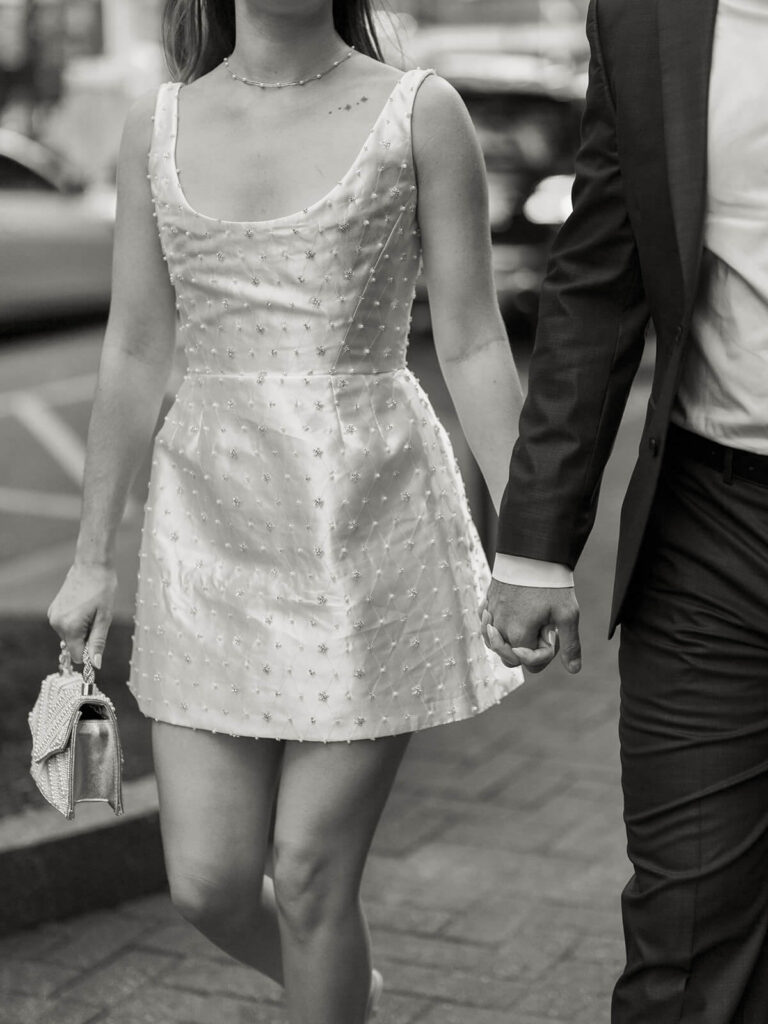 Couple holding hands walking on Charlotte street woman in white beaded dress man in dark suit