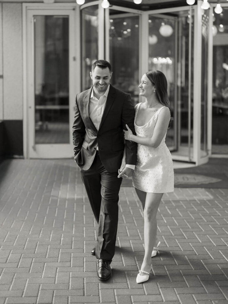 Black and white of couple walking and laughing outside restaurant uptown Charlotte engagement photos