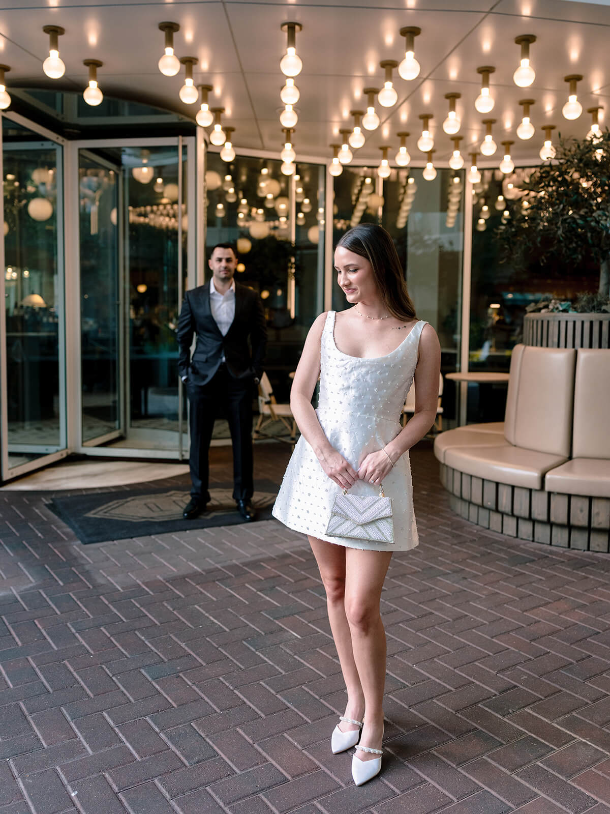 Woman in white beaded dress at hotel entrance with string lights Charlotte engagement session