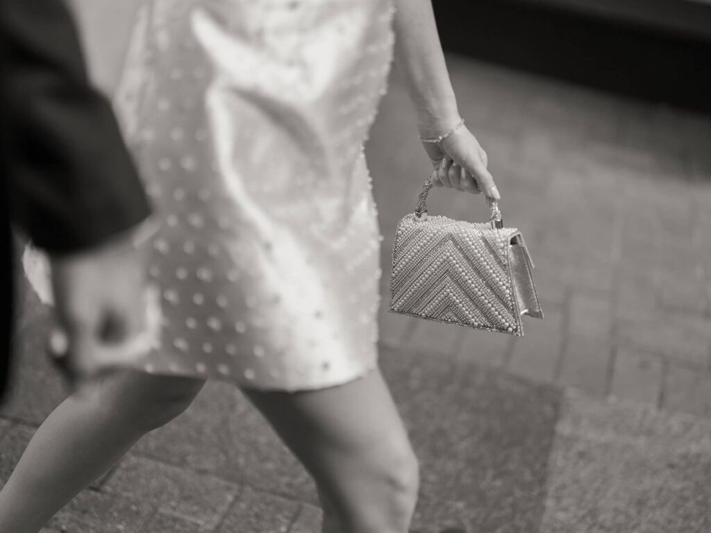 Black and white detail of woman in white dress walking with beaded handbag Charlotte engagement
