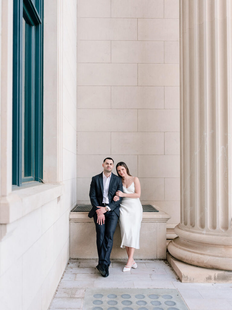 Wide shot of couple posing against stone wall between column and window Gandhi Park Charlotte