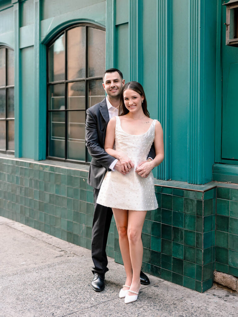 Couple embracing in front of teal-tiled building corner uptown Charlotte engagement photos