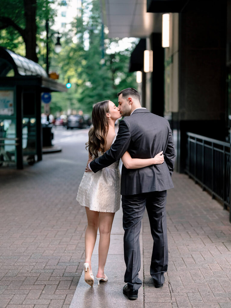 Couple kissing on tree-lined Charlotte sidewalk viewed from behind engagement session