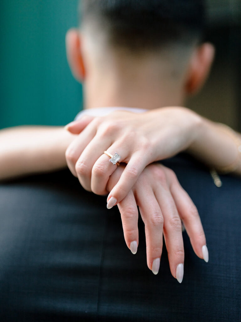 Close-up of woman's hands with emerald-cut engagement ring draped around man's neck Charlotte