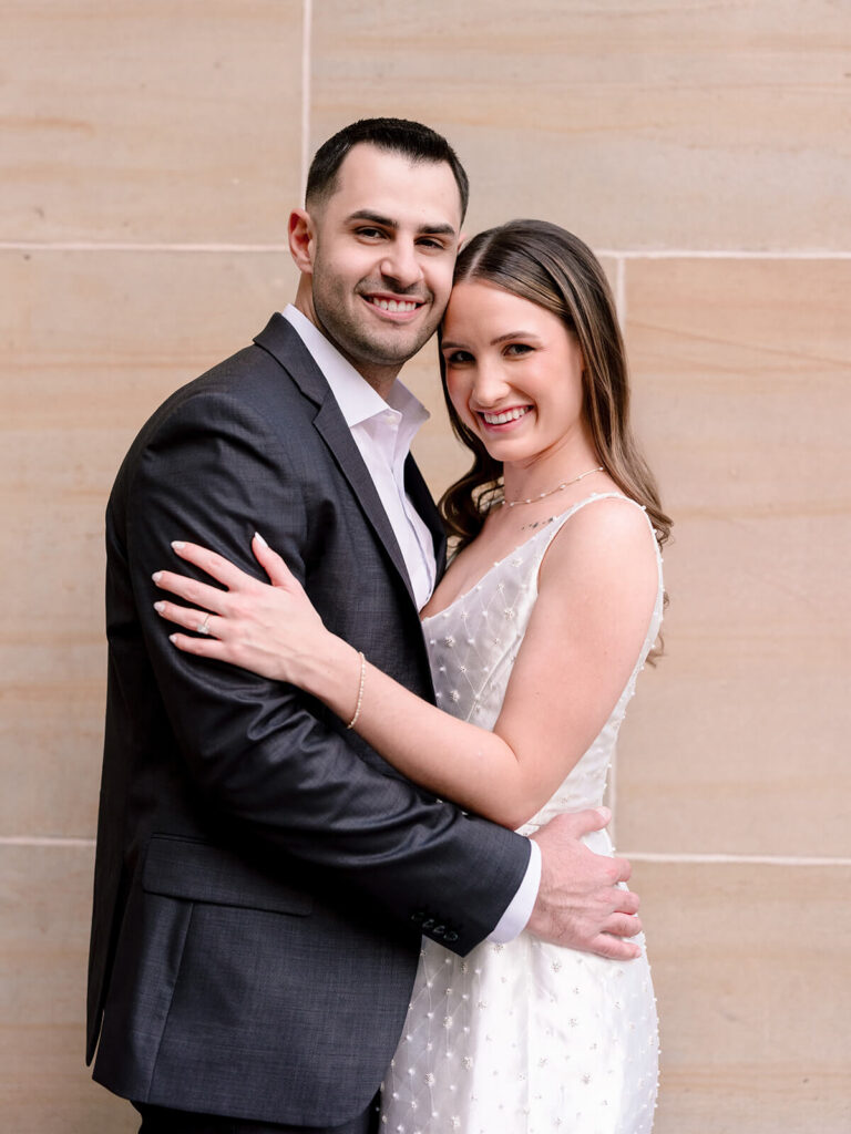 Close-up portrait of couple embracing against sandstone wall with engagement ring visible Charlotte