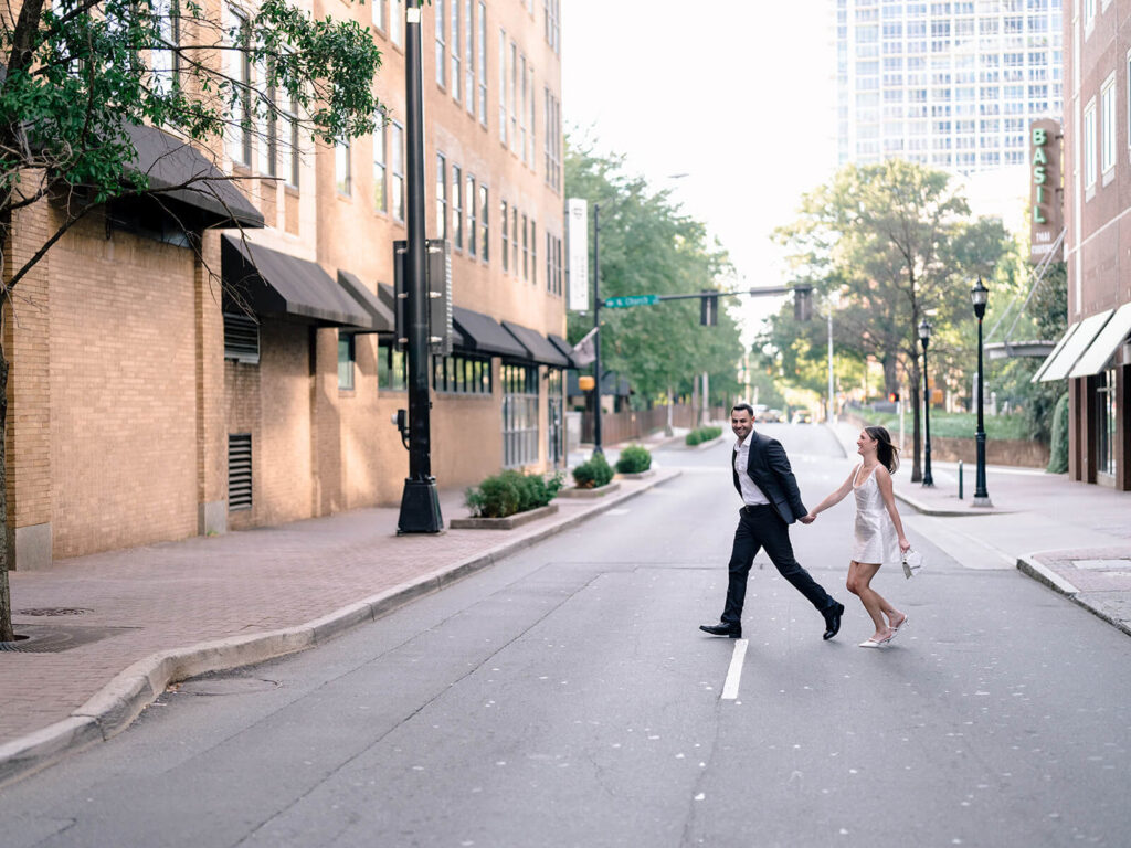 Couple crossing downtown Charlotte street holding hands man in suit woman in white dress