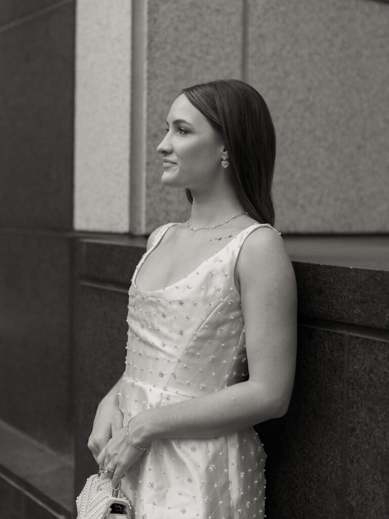 Black and white profile portrait of woman in beaded dress leaning against stone wall Charlotte