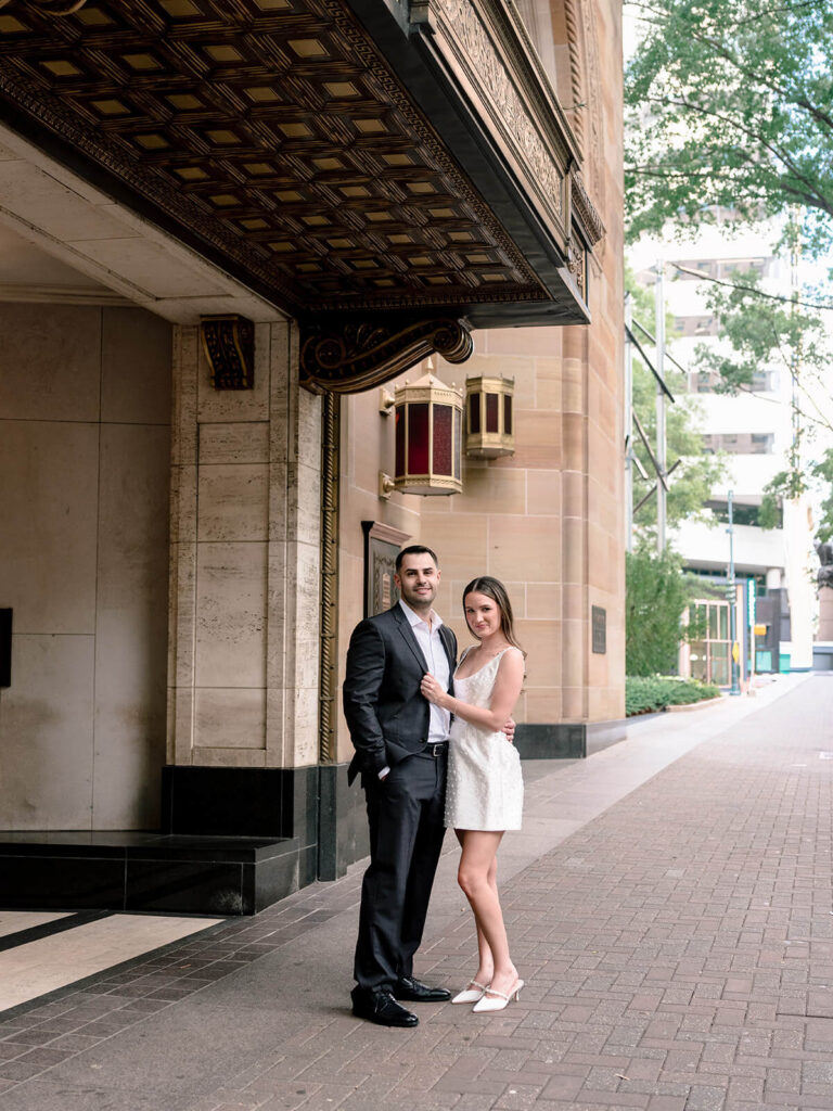 Couple posing under ornate bronze theater awning with vintage lanterns Charlotte engagement photos