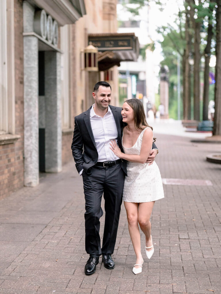 Couple walking arm-in-arm laughing on brick sidewalk with theater awning uptown Charlotte