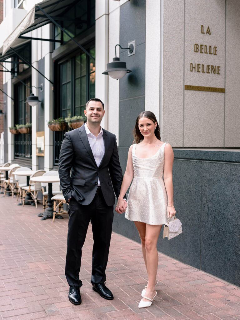 Couple holding hands outside La Belle Helene on Tryon Street uptown Charlotte engagement photos