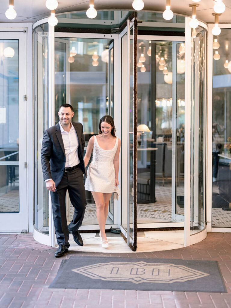Couple exiting through revolving glass door laughing during Charlotte engagement session