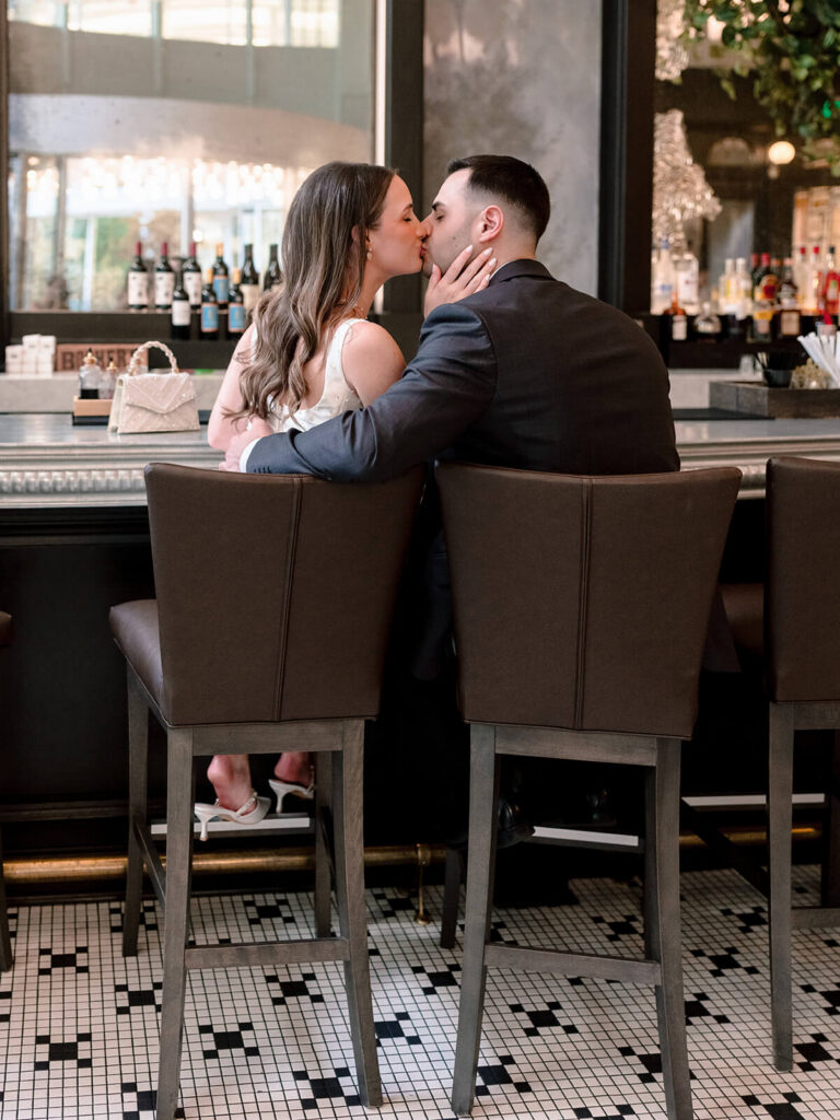 Couple kissing while seated at upscale bar black and white tile floor Charlotte engagement photos