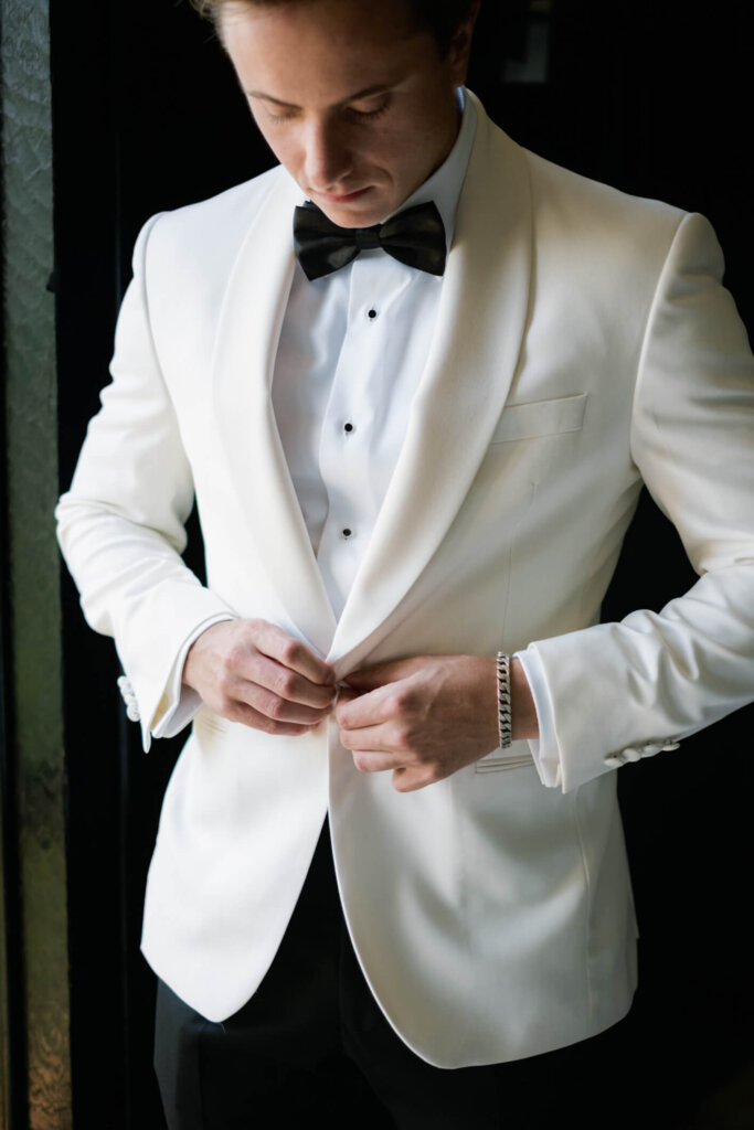 Groom putting on his white dinner jacket before the Bedford wedding outside NYC