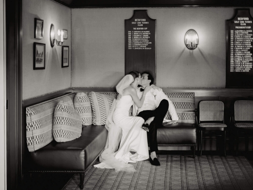 Bride and groom kissing on a leather sofa after the ceremony at Bedford Golf and Tennis Club