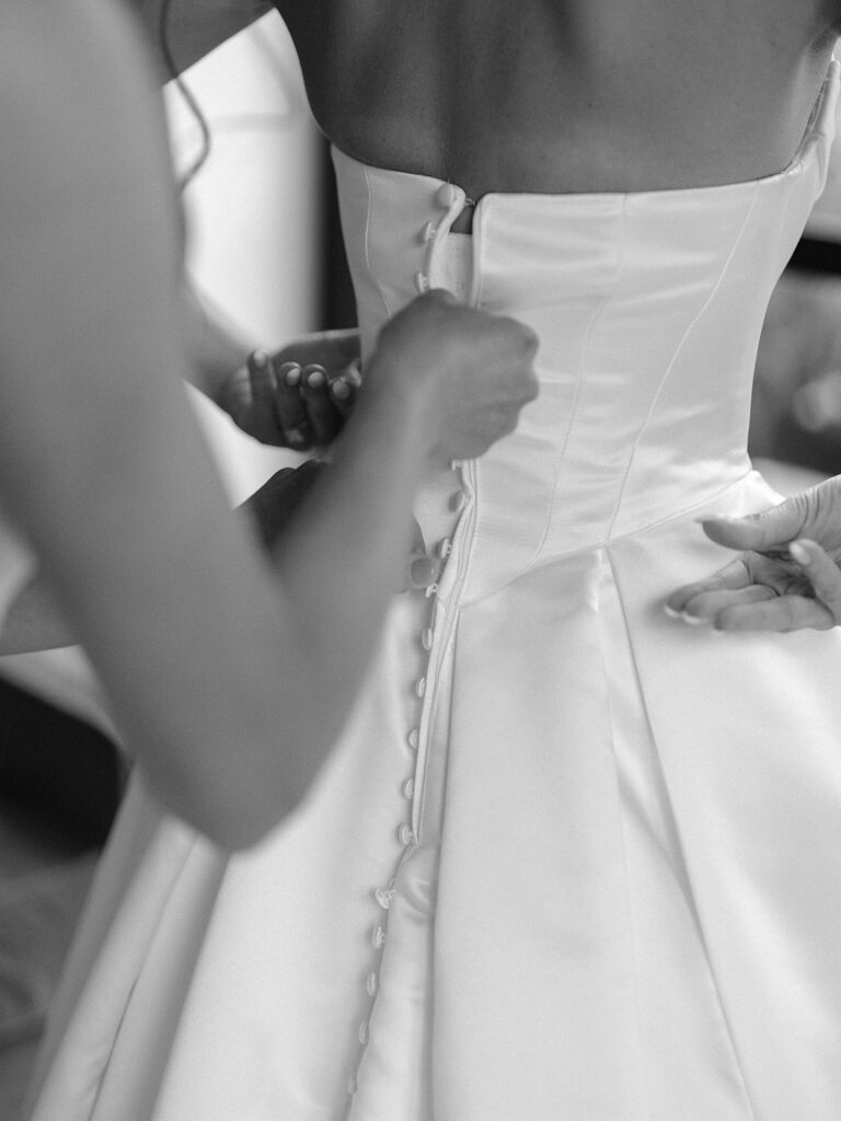 A bridesmaid buttoning the back of Tiffany's wedding gown