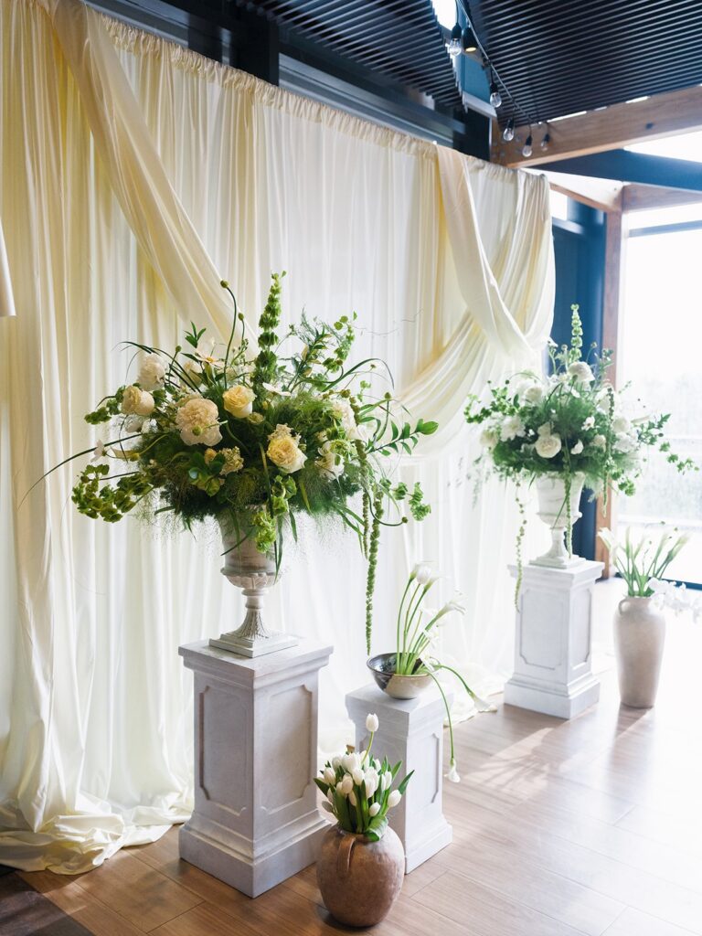 Green-and-white floral installation against white ceremony draping