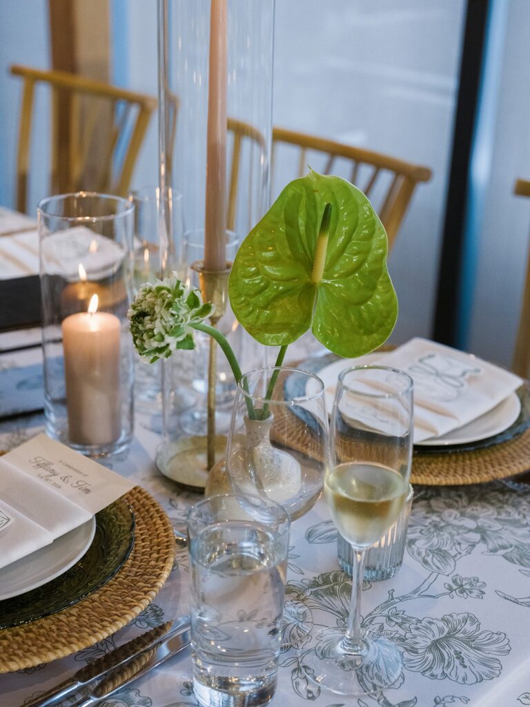 Green-and-white District Winery wedding place setting with anthurium, woven charger, and candlelight