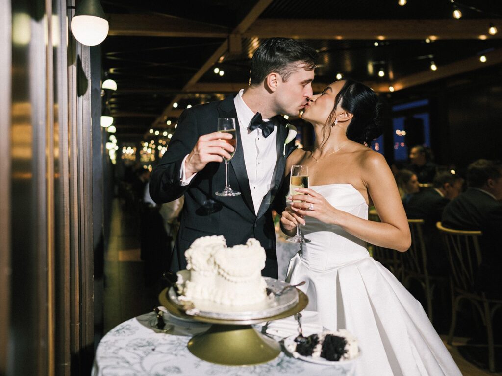 Tiffany and Tim kissing beside their white wedding cake