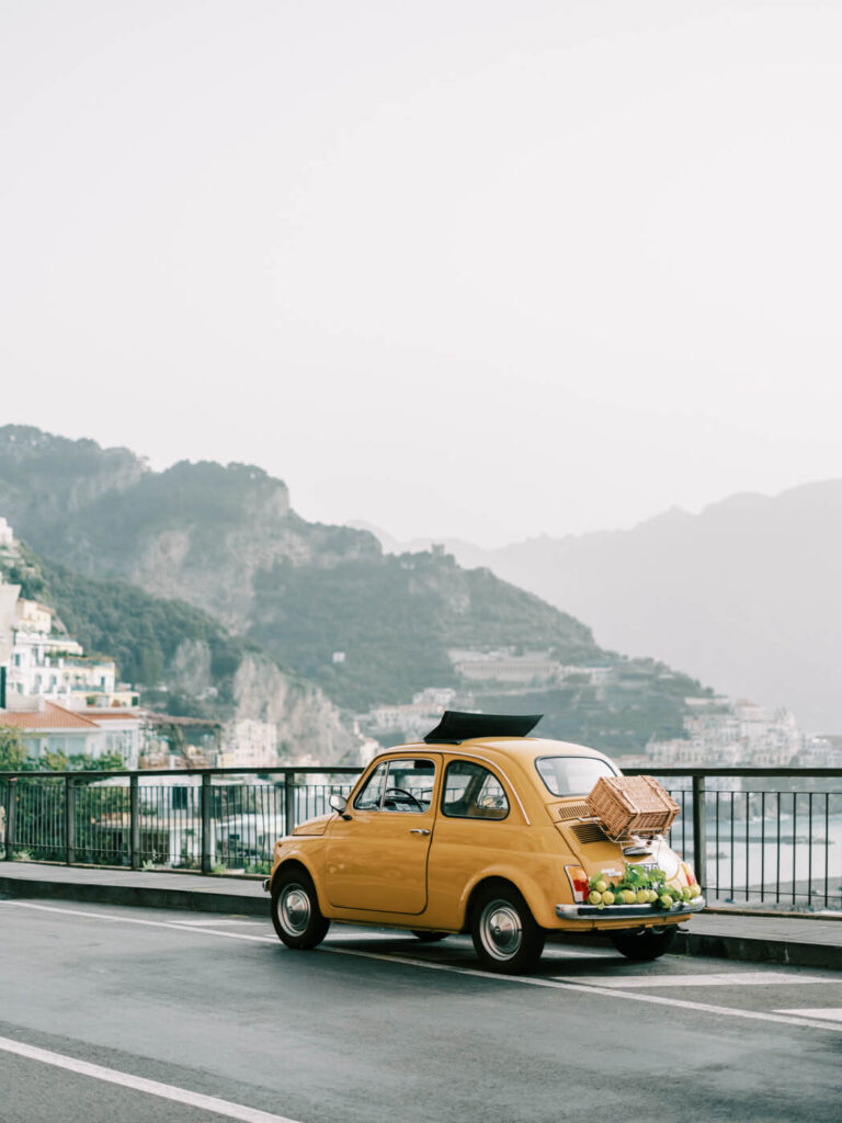 Vintage yellow Fiat adorned with fresh lemons, parked on the scenic roadside overlooking the Amalfi Coast.