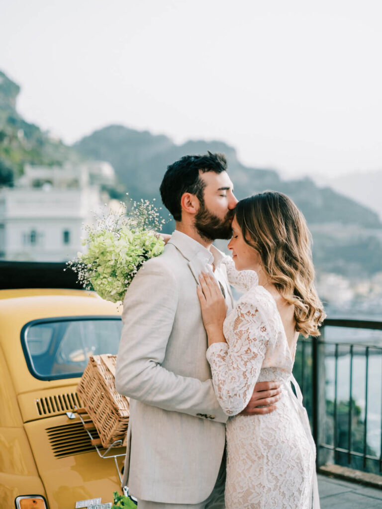 Alessandra and Alessio sharing a tender embrace beside their lemon-decorated Fiat during an Amalfi Coast couples session.