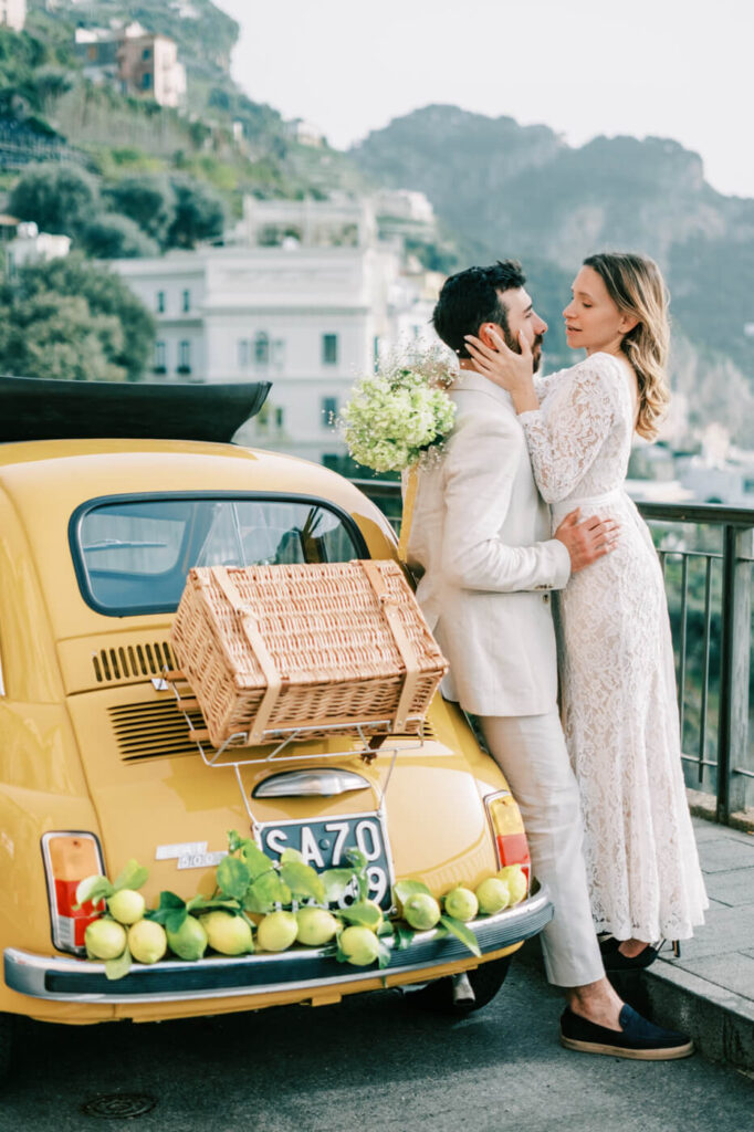 Bride and groom embracing beside their vintage car, with Alessandra’s bouquet adding a soft, romantic touch.