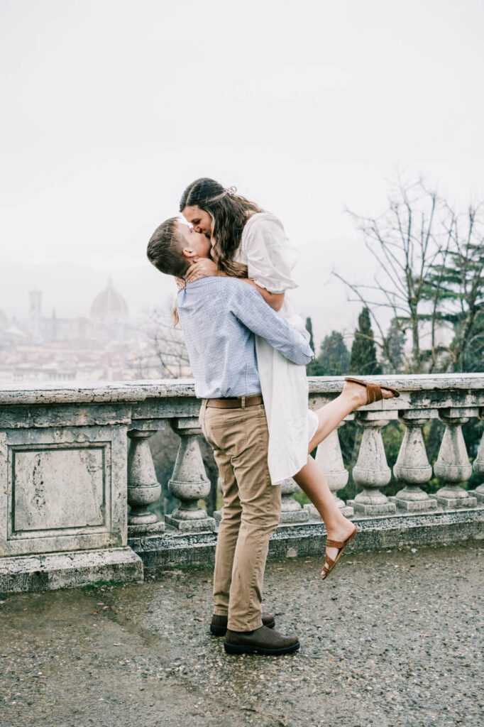 Playful couple moment with Florence skyline backdrop – The groom lifts the bride into a joyful kiss, with the iconic Florence cityscape and Duomo in the background.