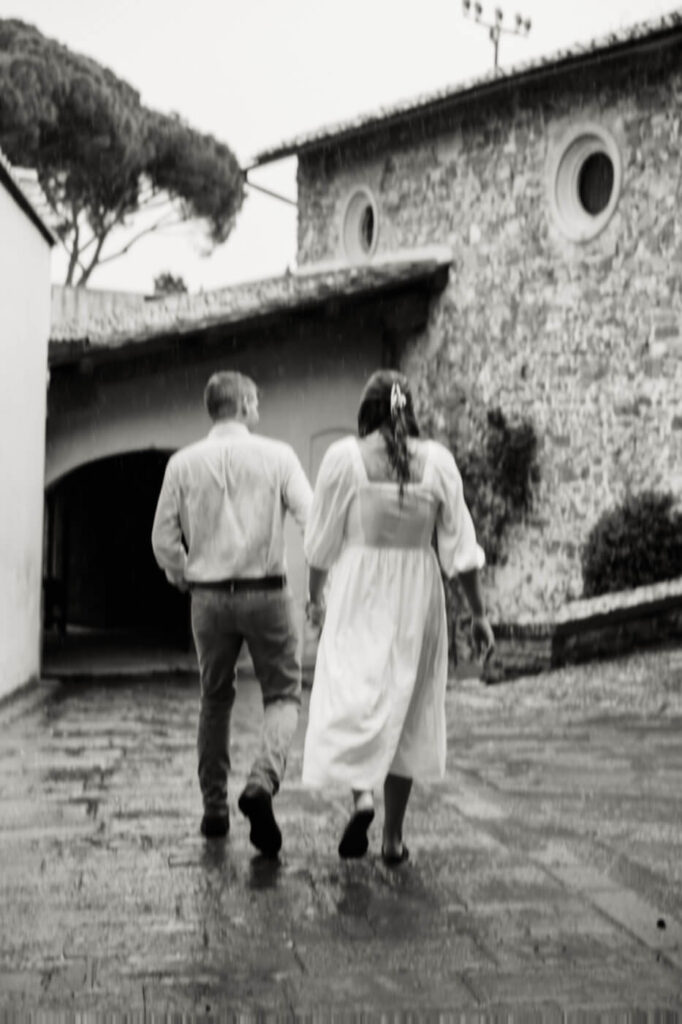 Couple walking hand in hand through historic Florence streets – A black-and-white image of the couple strolling down a wet cobblestone street, with raindrops adding a timeless, romantic touch.