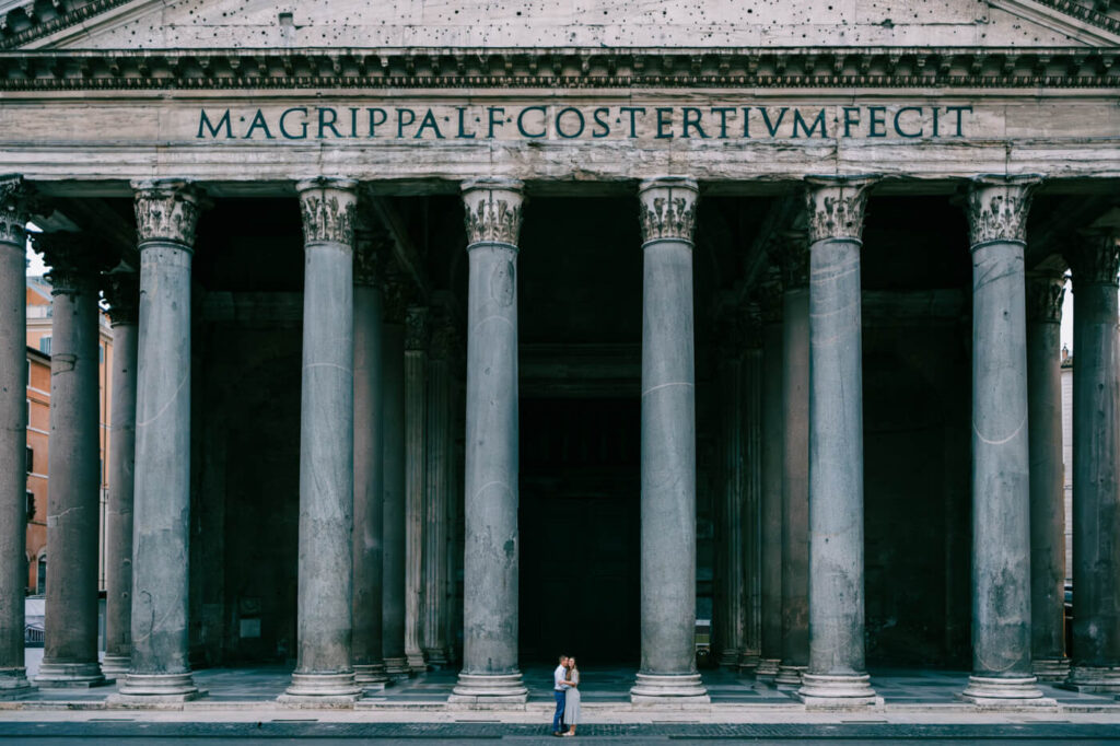 Couple at the Pantheon, Rome – A couple embraces in front of the grand columns of the Pantheon, with its historic Latin inscription visible above them, capturing a timeless moment in Rome.